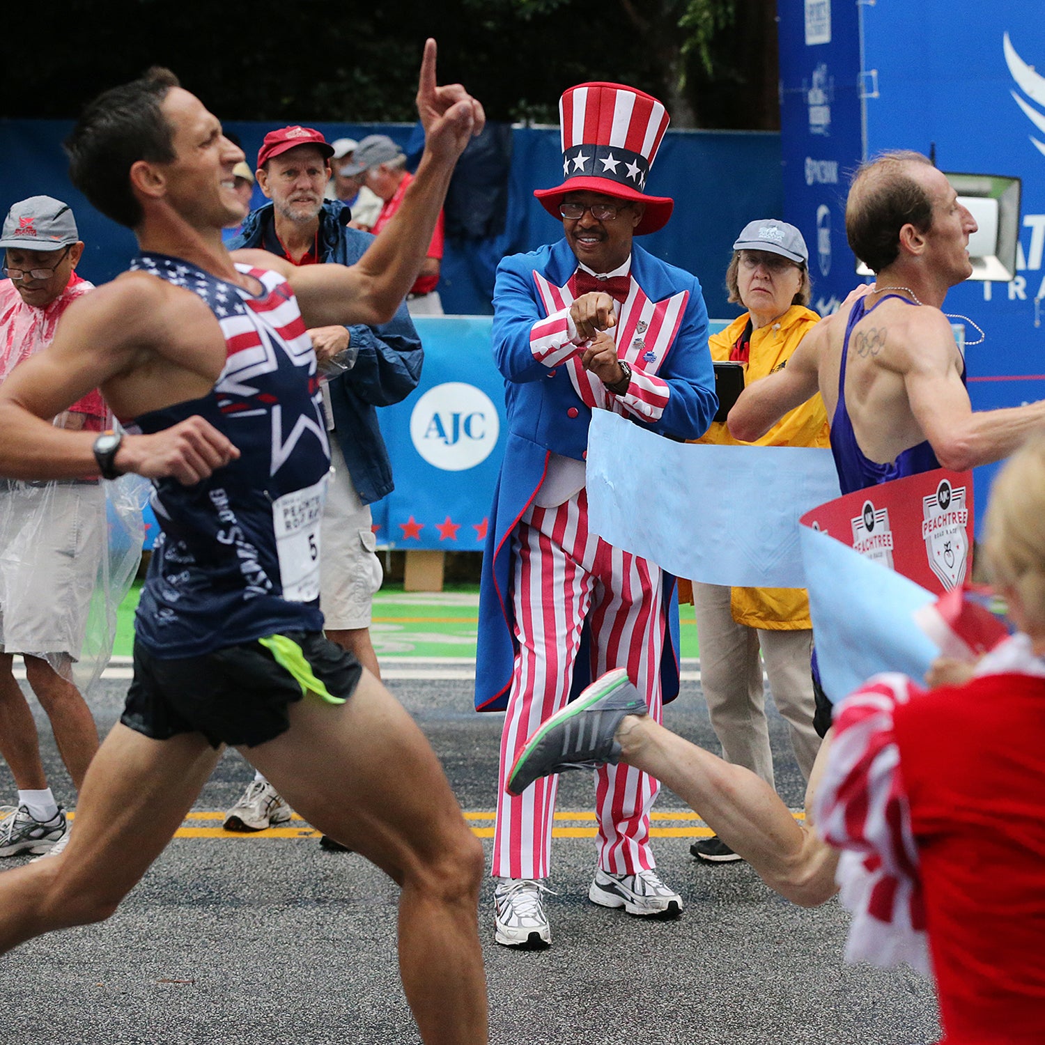 Scott Overall hits the tape, right, to win the men’s open division while runner Ben Payne comes in second place at the finish line of the AJC Peachtree Road Race on July 4, 2015.