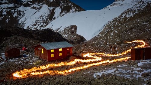 With petroleum as his paint, English photographer Simon Norfolk took to Africa’s second highest peak, Mount Kenya, to outline the mountains’ vanishing Lewis Glacier. Using old maps and meticulous GPS plotting, the fire lines represent an old section of the glacier, often a large distance from the glacier’s current front. Norfolk’s work, completed in 2014, is marked by grief but he hopes it also serves as a call to action. In his words, to think that “in ten or twelve years this magnificent glacier that has endured for millennia will exist only in photographs, is unbearable.”
Photo: Norfolk was born in 1963, the year of the glacier’s position depicted by this fire line. At that time only the small hut on the left existed. The larger structure with the lights on, called the Austrian Hut, was built in 1972 and served as Norfolk’s residence during this project in 2014.