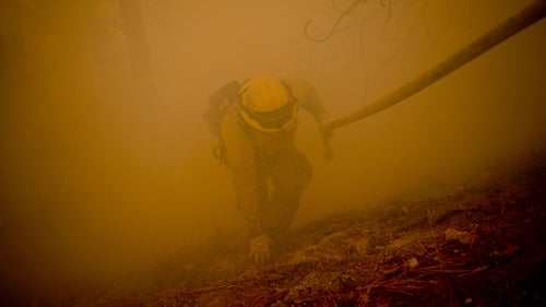 Big Bear City Firefighter Josh Mandolini uses a fire house to pull himself up a steep hillside while fighting the Slide Fire in Running Springs, California, on October 24, 2007.
