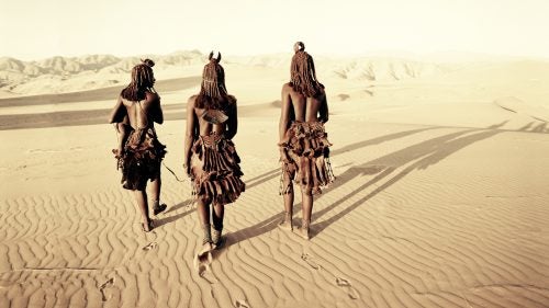 The Himba are an ancient tribe of an estimated 20,000 to 30,000 members located near the Kunene River in northwest Namibia and southwest Angola. They’re known for being tall, slender, and statuesque semi-nomadic herders. Most still live and dress according to ancient traditions and speak Herero—their language since the 16th century. The Himba live in scattered settlements of cone-shaped structures made of saplings bound together with palm leaves and plastered with mud and dung. If grazing is poor, the village will migrate to land with better opportunities, with young men leaving first to set up separate, temporary villages and move the cattle, while the women, children, and older men stay at the main settlement.