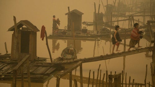 Wildfires of unprecedented size have been burning through the lush forests of Sumatra and Borneo in Indonesia since August. The government has no idea how to control them, and the mounting damages are staggering. The release of carbon dioxide, methane, and nitrous oxide gasses is more than triple the annual amount for the country, surpassing Japan and Germany in emissions, according to the Global Fire Emissions Database. Plus, El Niño is keeping rainfall away from the islands.
Greenpeace Southeast Asia alleges that the blazes were intentionally set by palm oil and pulp farmers carrying out slash-and-burn agriculture. Rampant draining of the swamp-like peatlands before the fires started has exacerbated the issue by effectively turning the areas into tinderboxes of dry organic material. The burns, which can reach as far down as ten feet below the surface, have sent large amounts of smoke into the air, blotting out sunlight and sending a haze as far as Malaysia and Singapore several hundred miles away. They’ve also reportedly caused over 500,000 cases of acute respiratory infections, according to Al Jazeera.
Greenpeace commissioned photographer Ardiles Rante to document just how severe the village of Sei Ahass in Borneo has been affected. The organization has also called for a halt to current logging, the re-flooding of drained peatland, and for publicly accessible mapping of current harvesting, which it has been linked to the greatest burned areas.
Photo: Two women carry buckets of silverware in Sei Ahass. “They go to the river to perform daily activities—washing dishes and clothes,” says Rodrigo Estrada, a media officer for Greenpeace U.S. “The little houses are owned by each family.”