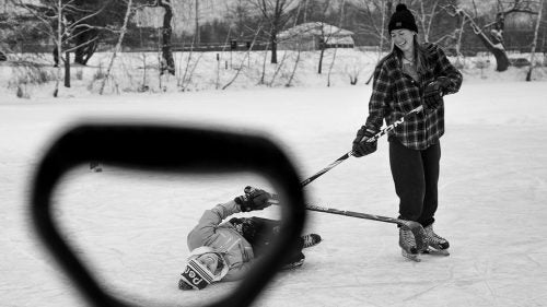Two Colby students are shown through the handle of a shovel used to clear the ice. Though the game was competitive, the atmosphere was decidedly lighthearted. “The whole point was to balance the teams and just try to get the level of the game as high as possible,” Wynia says. “It seemed to be a battle against winter—getting your heart rate up on a freezing afternoon—more than anything.”