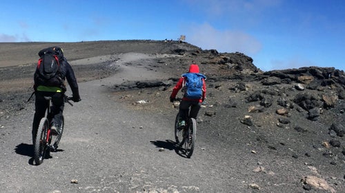 Summit day was the coldest morning yet—frost blanketed everything in sight. With our bikes attached to our backpacks, we started hiking up the toughest section. It was a fierce, nearly vertical vein of scree, rocks, and volcanic material leading from high camp to the crater's rim that is Kilimanjaro’s highest point.
The first two-and-a-half hours in the dark were tortuous. Around 17,500 feet was my worst point. I was struggling to take in air as we scrambled up near-vertical scree for hours. The sun rising over the distant Miwenze peak to the east was a welcome friend, outlining the wild ridges in bright pink and orange. When our suffering was at its worst, our guide, Respicius Baitwa, would break into song, bringing a smile to our faces and reminding us to enjoy the journey.
Finally we reached Gillman's point, on the east side of the crater’s edge. Next stop would be Stella Point, at 19,000 feet, and the final push to the summit.