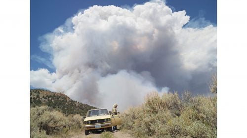 George chasing wildfires; Eureka, Nevada, 2012.
I met George in Diamond Valley, Nevada. He raised cattle for most of his life, but in his retirement, George enjoys chasing forest fires. We drove on dirt roads with dust coming up through the floor of his truck, and then stopped at this hill with fire burning on the other side. He told me very confidently that he had safety provisions. I asked what kind. He said, “I have two bottles of water, a Coke, a candy bar, a shovel, and a handgun.”
Wildfires remove underbrush and kill diseases and insects, sparking new growth and allowing established trees to grow stronger. But the frequency of wildfires and the length of the wildfire season have been increasing. Since 1960, only seven years have seen more than 8 million acres burned in the United States, according to National Interagency Fire Center records. All of those years were in the past decade.