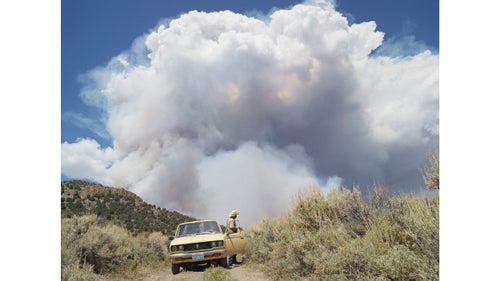George chasing wildfires; Eureka, Nevada, 2012.
I met George in Diamond Valley, Nevada. He raised cattle for most of his life, but in his retirement, George enjoys chasing forest fires. We drove on dirt roads with dust coming up through the floor of his truck, and then stopped at this hill with fire burning on the other side. He told me very confidently that he had safety provisions. I asked what kind. He said, “I have two bottles of water, a Coke, a candy bar, a shovel, and a handgun.”
Wildfires remove underbrush and kill diseases and insects, sparking new growth and allowing established trees to grow stronger. But the frequency of wildfires and the length of the wildfire season have been increasing. Since 1960, only seven years have seen more than 8 million acres burned in the United States, according to National Interagency Fire Center records. All of those years were in the past decade.