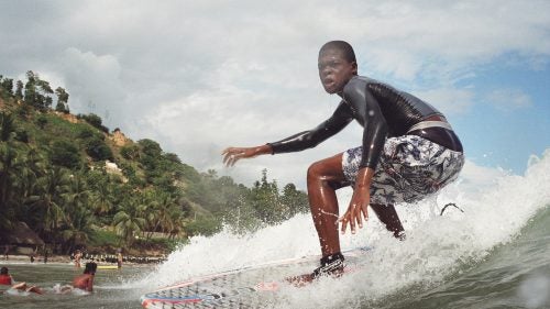 Another one of Surf Haiti’s top contenders catches a small wave in shallow water.