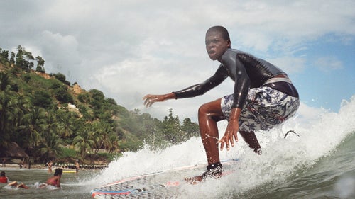 Another one of Surf Haiti’s top contenders catches a small wave in shallow water.