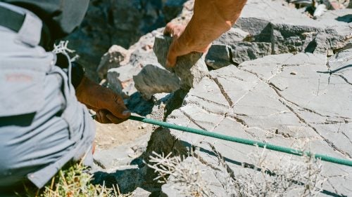 Swaney smooths a sharp rock lip so it won’t cut the rope. Cyclops Canyon, May 3, 2016.
So many things can go wrong that when I am finally leaning backwards over the edge of my very first canyoneering rappel, I have to adopt a mind-set of pure faith. Behind me is a 160-foot drop. In front of me is a gnarled knee-high tree with a loop of webbing around it. I trust Swaney. I trust Plummer, who has already descended this section and is waiting below, backing me up with a fireman’s belay. I trust the others and their decades of combined experience. I trust this tiny tree. And I do trust myself to stay calm and execute a proper rappel. Swaney reminds me to never, ever let go of the brake rope in my right hand. Otherwise, I’ll zip straight down the line and die on impact.