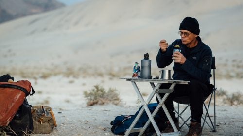 Swaney eating breakfast below the Eureka Dunes. May 21, 2016.
I learned about Swaney from a good friend who’s been following him on Facebook, fascinated by stories and photos of huge rappels, remote natural bridges, slick rock dryfalls, and rattlesnakes. My friend and I have been exploring Death Valley regularly for 15 years, and we’ve had many hikes end abruptly at the foot of an impassible canyon dryfall.
I reached out to Swaney via Facebook, and he quickly replied within minutes with a thumbs-up emoji. Then: “You will have to join up. Been going every weekend this season. Lots of new canyons to check out.” One month later, I’m riding in his dust-coated Nissan Pathfinder, heading from Los Angeles to Death Valley, while he gives me lessons on rappelling.
