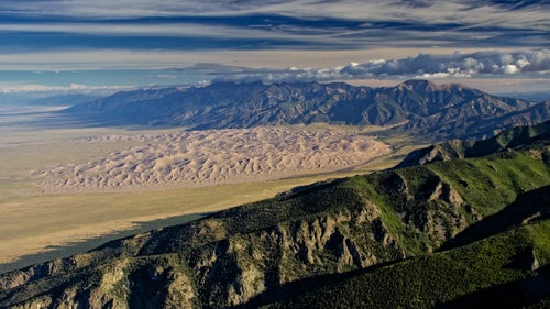 When I was young, I had a habit of poring through national park books, fantasizing about visiting them all. Now I’m a part-time aerial adventure photographer, and I’ve been able to fly my Piper PA-11 Cub Special plane over many of the places I used to daydream over.
In a few instances, I have made it a point to fly over a park. But many of my best national park shots happen on unplanned trips. While in pursuit of another item to photograph from the air, I happen to find myself flying through one of the national parks. Distraction takes over and I forget about my initial project.
Since we’re celebrating the national parks centennial, these are some favorite shots that I’ve taken over the last four years. I like the aerial perspective as it’s a fast track to seeing the full magnitude of a park’s beauty. I continue to find unbelievable hidden places inside the park system from the air.
Photo: On this particular morning in September 2015, I was hoping to photograph nine peaks over 14,000 feet (five of them are viewable on the horizon where the clouds touch the peaks). Approaching from the airport in Alamosa, Colorado, the entire scene was shadowed by the rising sun, and I was convinced the entire exercise was going to be a waste of time. As I rode the winds to gain altitude over the Sangre de Cristo Range foothills, attempting to get a good angle on four fourteeners behind me, this panorama opened up.