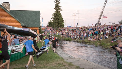 Fans cheer on the start of the Au Sable River Canoe Marathon as racers dash into the river.