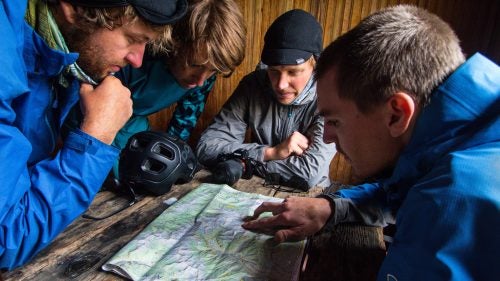 (Left to right) Kraushaar, Simmons, Stucki, and Trevor Downing take refuge from the monsoon weather in a small mining cabin. The crew studies the upcoming day’s routes, hoping for sun and hungry trout.