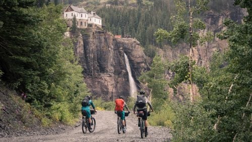 Spend ten days ripping singletrack and fly fishing through Colorado’s San Juan Mountains with a group of your best friends and you might just have a dream vacation. This August, photographer and rider Ben Kraushaar put together a crew of MTB and adventure junkies to do just that. With Telluride as the jumping off point, Kraushaar was joined by Justin Reiter, Dylan Stucki, Sam Simmons, and Trevor Downing for some high country trout, great riding, and plenty of challenging Colorado weather. Here, Kraushaar shares some favorite shots from their San Juan mission.
Photo: (Left to right) Sam Simmons, Justin Reiter, and Dylan Stucki pedal towards Bridal Veil Falls, the tallest waterfall in Colorado, in Telluride. We started our ten-day bikepacking trip in Telluride with the intention of fishing numerous alpine lakes and streams on our course through the San Juan Mountains.