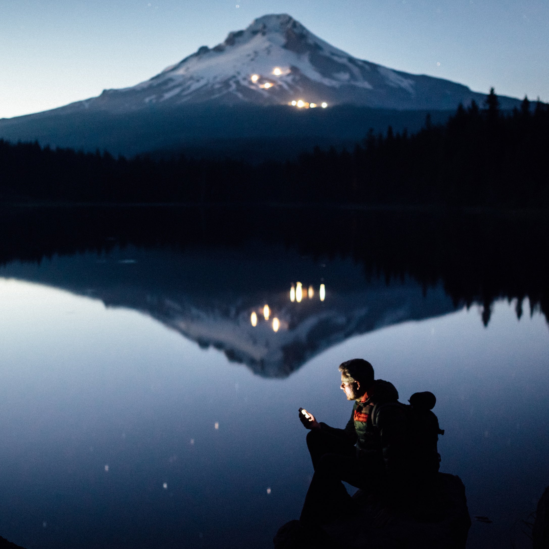 Hiker plugs in on a lake shore in Oregon at twilight.