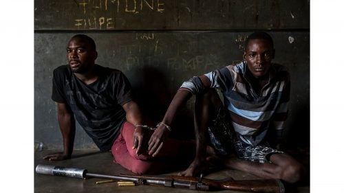 Nature - First Prize, Stories, Title: Rhino Wars
Two rhino poachers, one 19, the other 28 years old, apprehended by an anti-poaching team in Mozambique close to the Kruger National Park border. They are seen waiting to be processed in the local jail. After a three-day chase, they were caught in a roadblock and the rifle seized shortly thereafter. This was due to a coordinated effort between Kruger National Park in South Africa where the poachers intended to shoot rhino for their horns; and Sabi Game Park, a conservancy on the Mozambique side. The poachers were tracked and identified by their unique shoe pattern. They tried to say they had been on their way to buy cattle, but had no money on their persons, and, when asked, the alleged cattle owner said he did not know anything about selling his cattle. Authorities also seized a Czech CZ .458 hunting rifle, complete with a professionally built silencer. Both men admitted their guilt and will be charged under a new law which states that possession of the weapon and bullets indicates intent to poach rhino. This carries a maximum sentence of 12 years and/or $80,000. Their Toyota Hilux vehicle was also confiscated. The younger of the two poachers later led police to the homes of suspected weapons and transport suppliers, higher-ups in the rhino poaching syndicates known as level twos and threes. Those men had fled by the time the police arrived, but significant information was discovered in the form of identity documents, both real and forged, as well as banking account information.