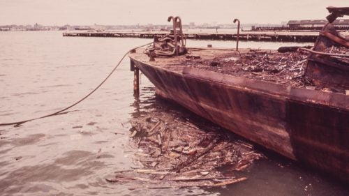 A rusting barge deposits debris in the Hudson River near the newly built World Trade Center in Lower Manhattan, 1973.