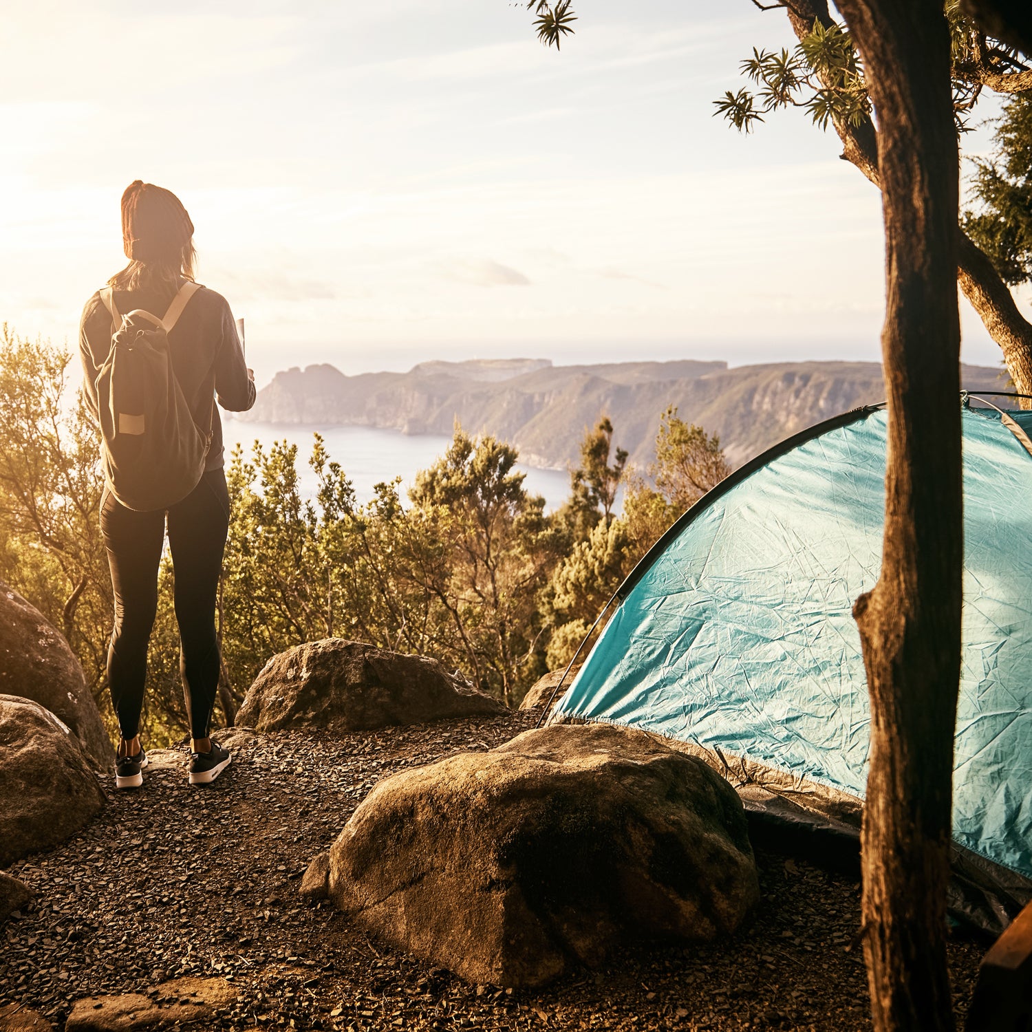 Shot of a young hiker enjoying the view of the ocean from a lookout while camping