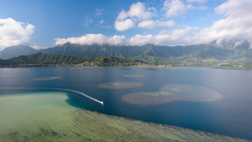 The windward coast of Oahu is world-renowned for its scenic vistas. The commanding peaks of the Ko’olau Range are the cornerstone of these famous views, dwarfing the communities that lie at their base. Pictured here, a boat motors through Kāne’ohe Bay on a calm morning inside the extinct Ko’olau volcano.
