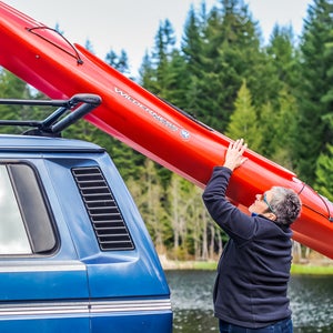 A woman loads her kayak onto her vehicle, using Yakima's ShowBoat—a load-assist boat carrier.