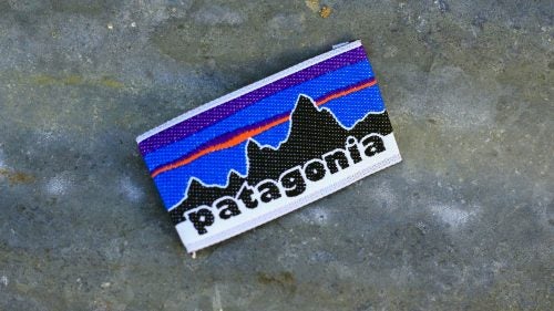 Original Patagonia Logo
According to Patagonia freelance artist Jocelyn Slack, the magic of a logo is that it’ll work if it makes the client “feel” what’s in their head. “I felt like the core collaboration was between me and Yvon, because he definitely had an idea of what he wanted. When he saw what he wanted, that was it.”
Chouinard wanted a logo for the clothing division. It was between “Patagonia” and “The Great Pacific Iron Works,” the name of their retail store. Slack was assigned the Patagonia logo and another artist the GPIW logo. Slack remembers feeling like the two artists were pitted against one another.
For inspiration, Chouinard gave Slack a climbing guide to the Fitz Roy Range of the Patagonian Andes. “So there were these old black-and-white photos, some with routes and descriptions of Fitz Roy. I did these pencil drawings of the mountains…and the big silhouette, and I think he was the one that maybe wanted some color. At one point, CEO Kris McDivitt mocked up a bunch of fonts spelling Patagonia. She asked Vincent Stanley his opinion one day, and he said the logo looked like Macy’s or Bloomingdale’s, and she threw it at him. ‘Patagonia Patagonia Patagonia’ all over the place. They kinda hashed it out, picking a font.”
The logo was first used in the Spring 1976 collection.