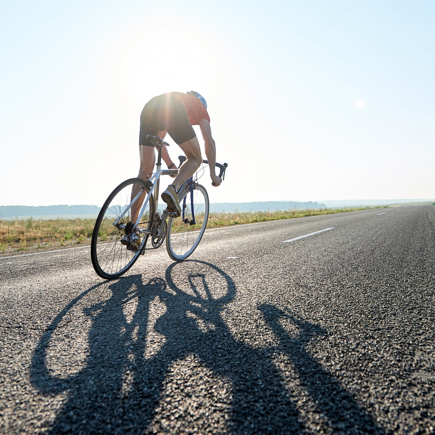 Rear view of sportsman riding bike on roar in sunlight, he participating in competition