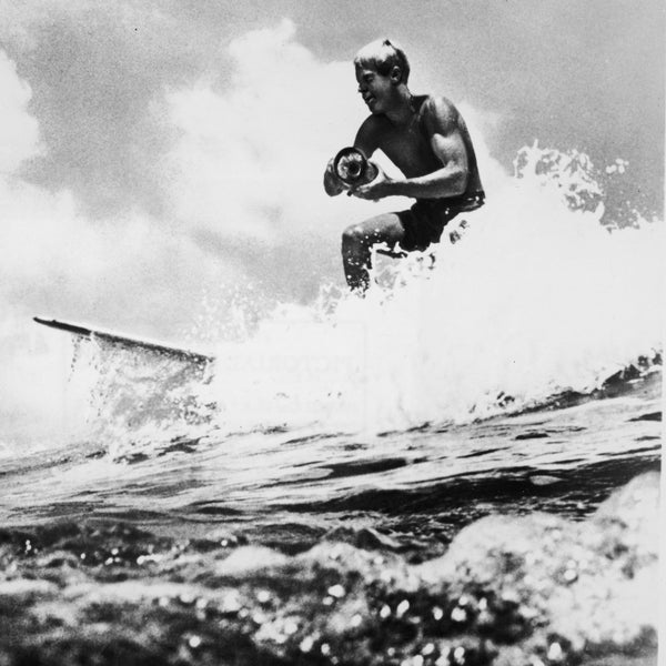 American surfer and director Bruce Brown surfs a wave and holds a camera while filming footage for his international surfing documentary, 'The Endless Summer,' circa 1966.