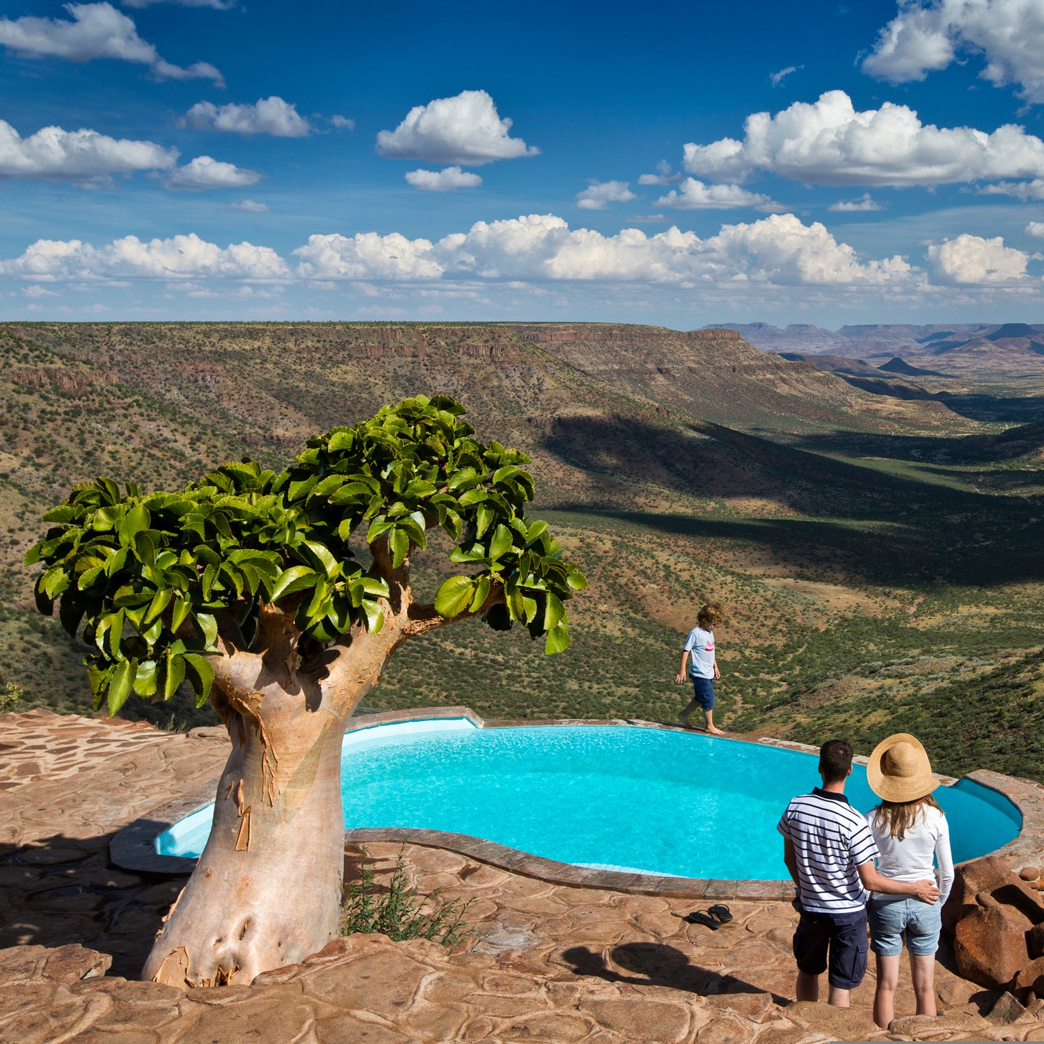 A couple stands at the Grootberg Lodge swimming pool looking out into the Klip River Valley, Damaraland, Namibia.