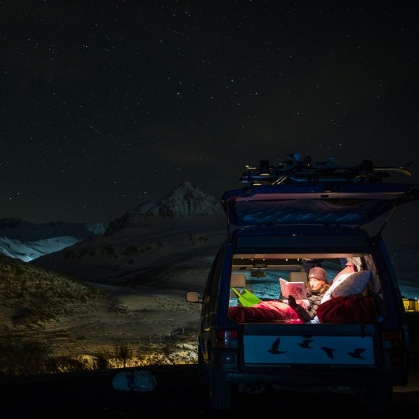 Chica viajando en furgoneta pasando noche bajo estrellas en invierno, tapada con un saco de dormir.