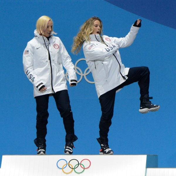 Kikkan Randall and Jessie Diggins do a podium dance after winning gold in cross-country skiing.