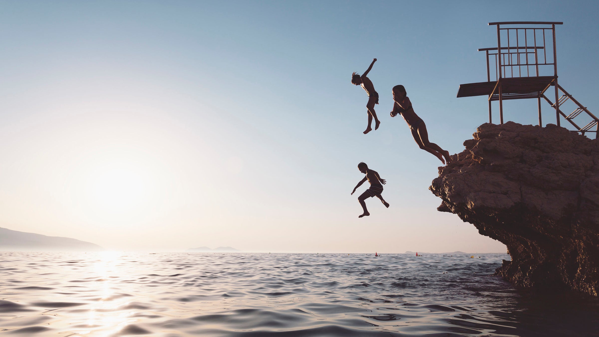 Silhouette of a group of children jumping from a cliff.