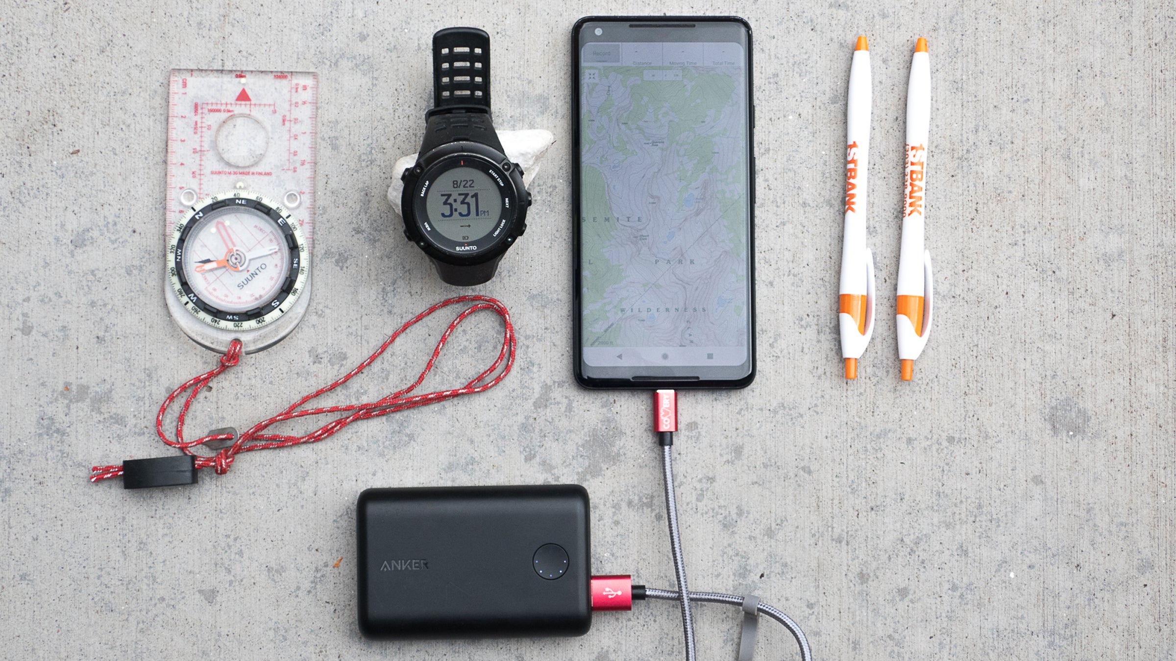 The author’s preferred system of navigation equipment: a magnetic compass, GPS watch, smartphone with a GPS app (plus a charger on longer trips), and two pens