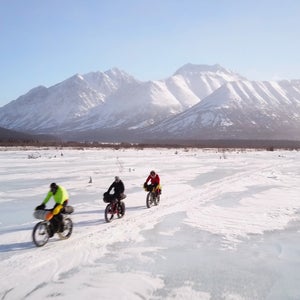Three riders leave the Rohn checkpoint riding across the Kuskokwim River