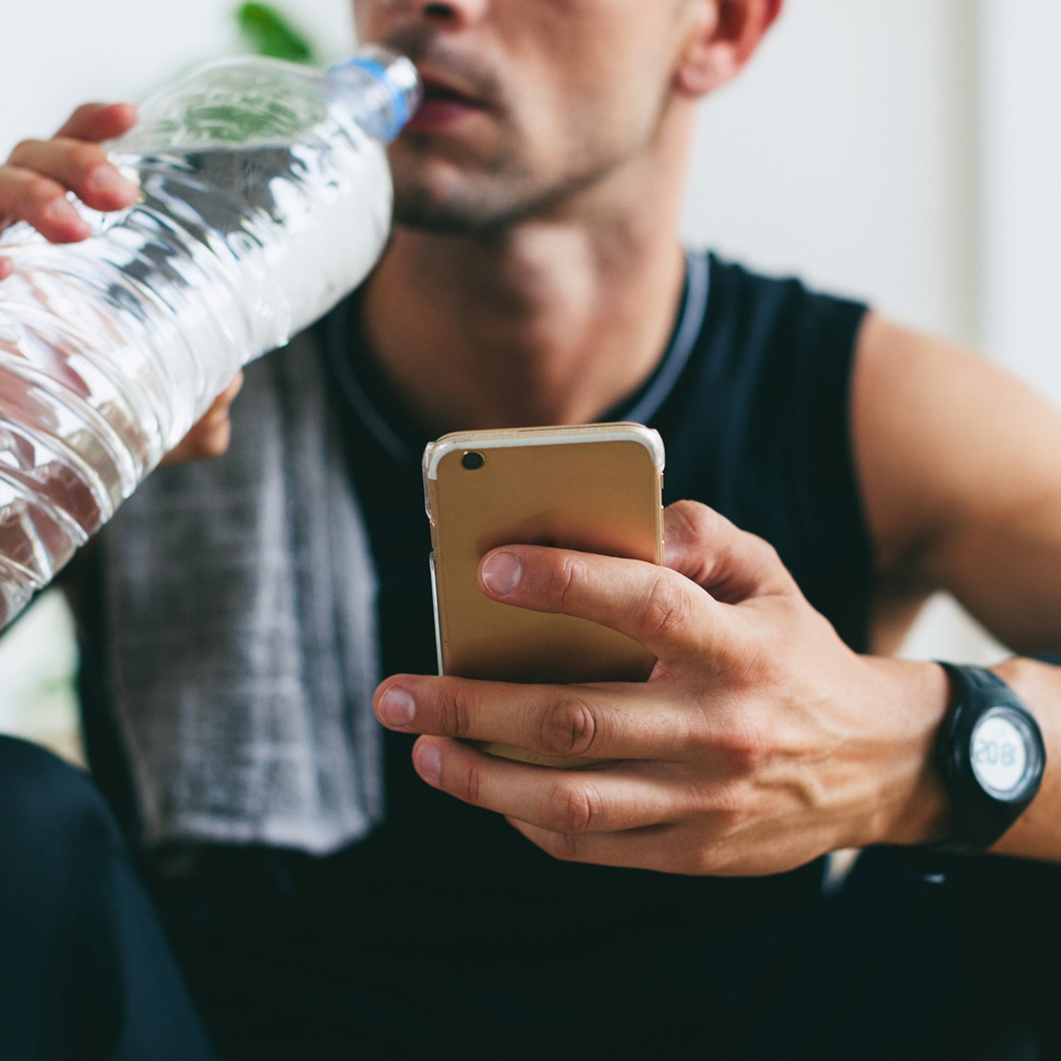 Closeup Of A Man Using His Phone Whilst Drinking Water After Hard Workout.