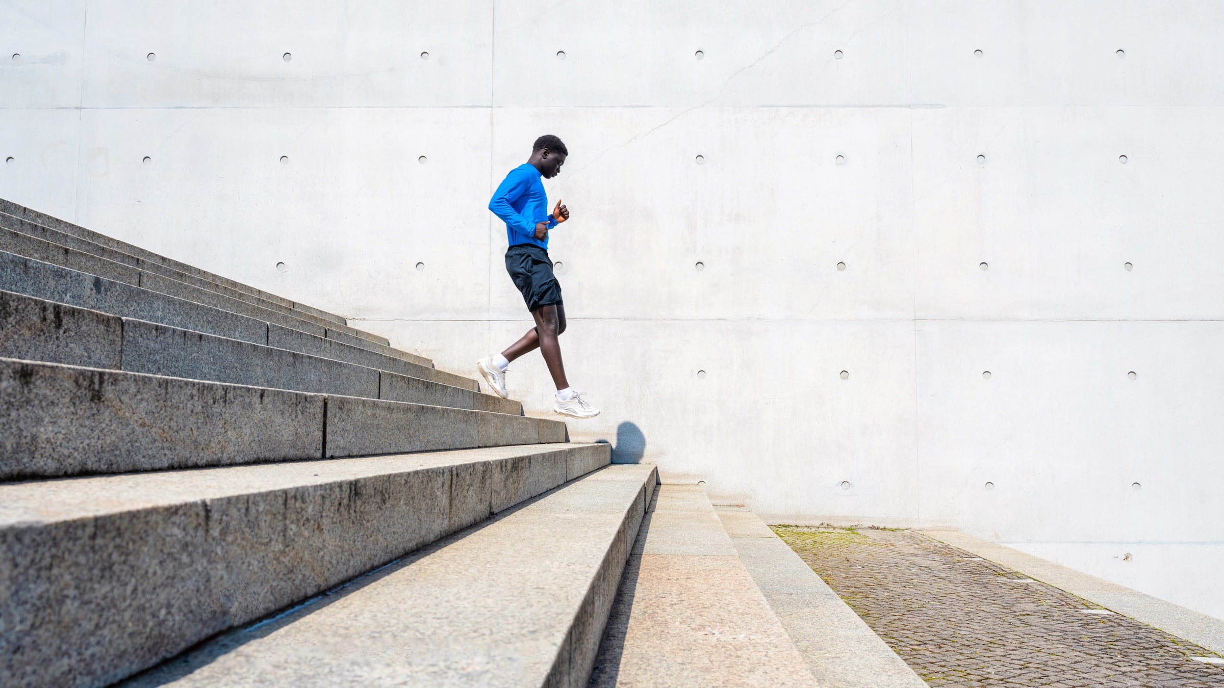 young sportsman running down steps in front of concrete wall outdoors in berlin at sunny day
