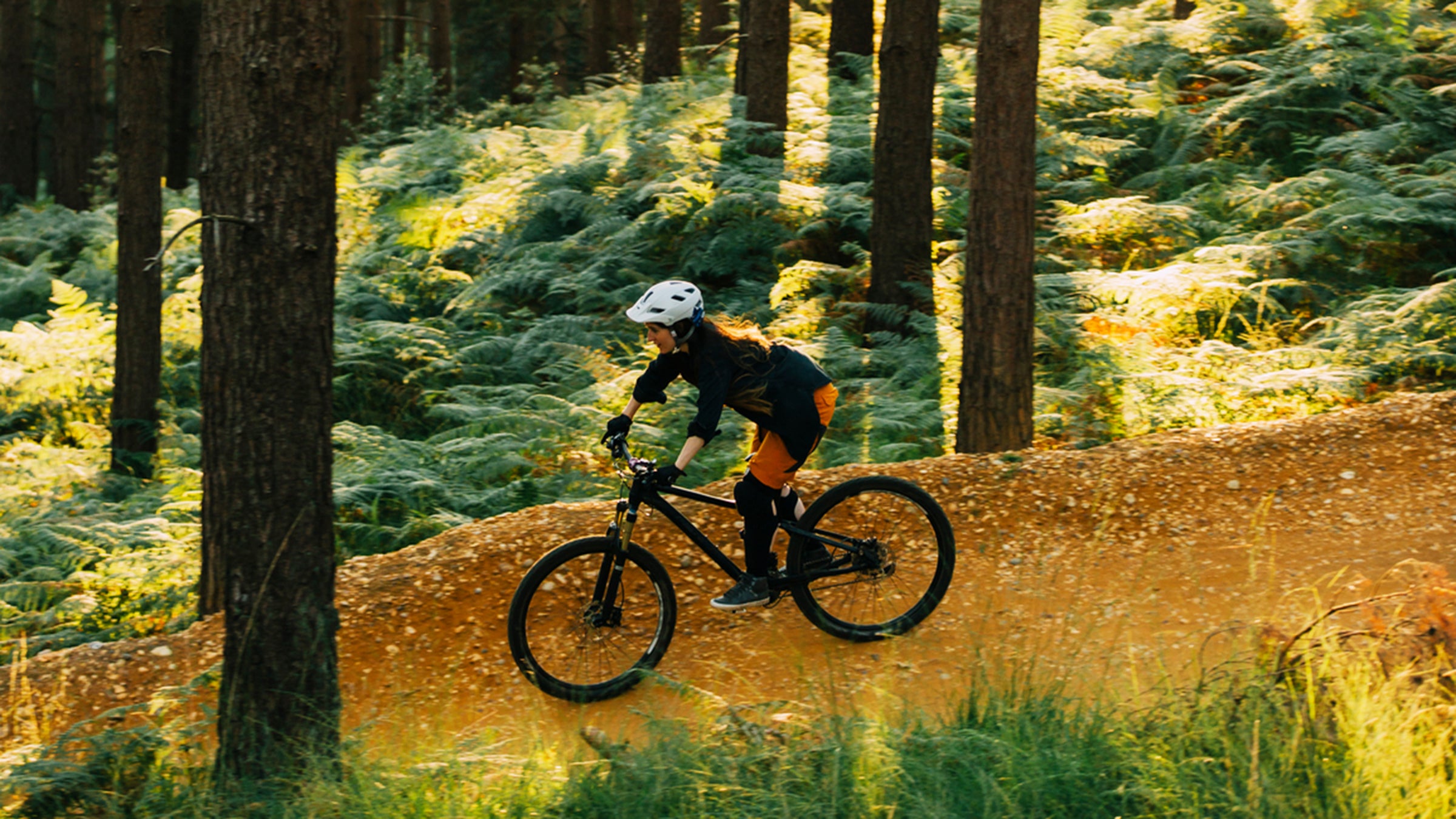A Woman Cycling Down A Sandy Forest Path At Sunset