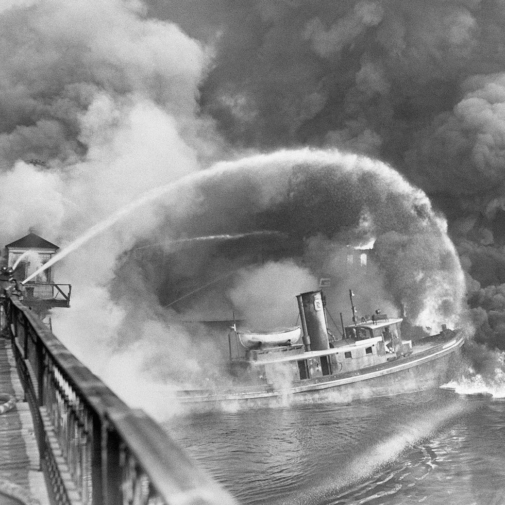 From November 3, 1952: Firemen stand on a Cleveland bridge over the Cuyahoga River, spraying water on the tug Arizona, as a fire, started in an oil slick, swept the docks at the Great Lakes Towing Company site on November 1. The blaze destroyed three tugs, three buildings, and the ship-repair yards.