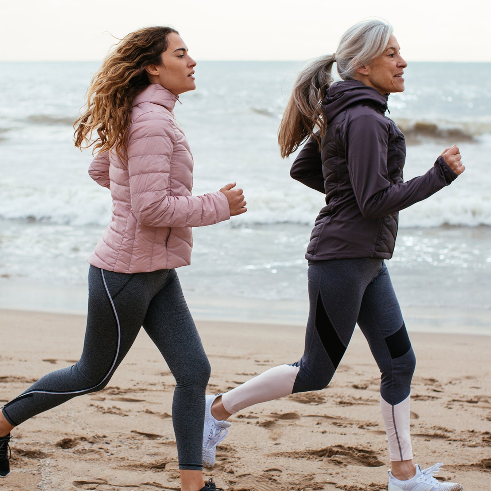 Senior Woman And Her Daughter Running On The Beach.