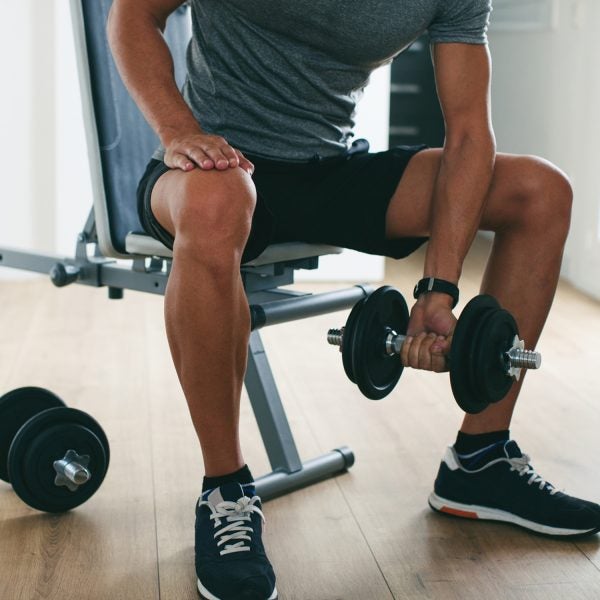 Closeup Of A Man Lifting Weights Sitting On A Workout Bench At Home.