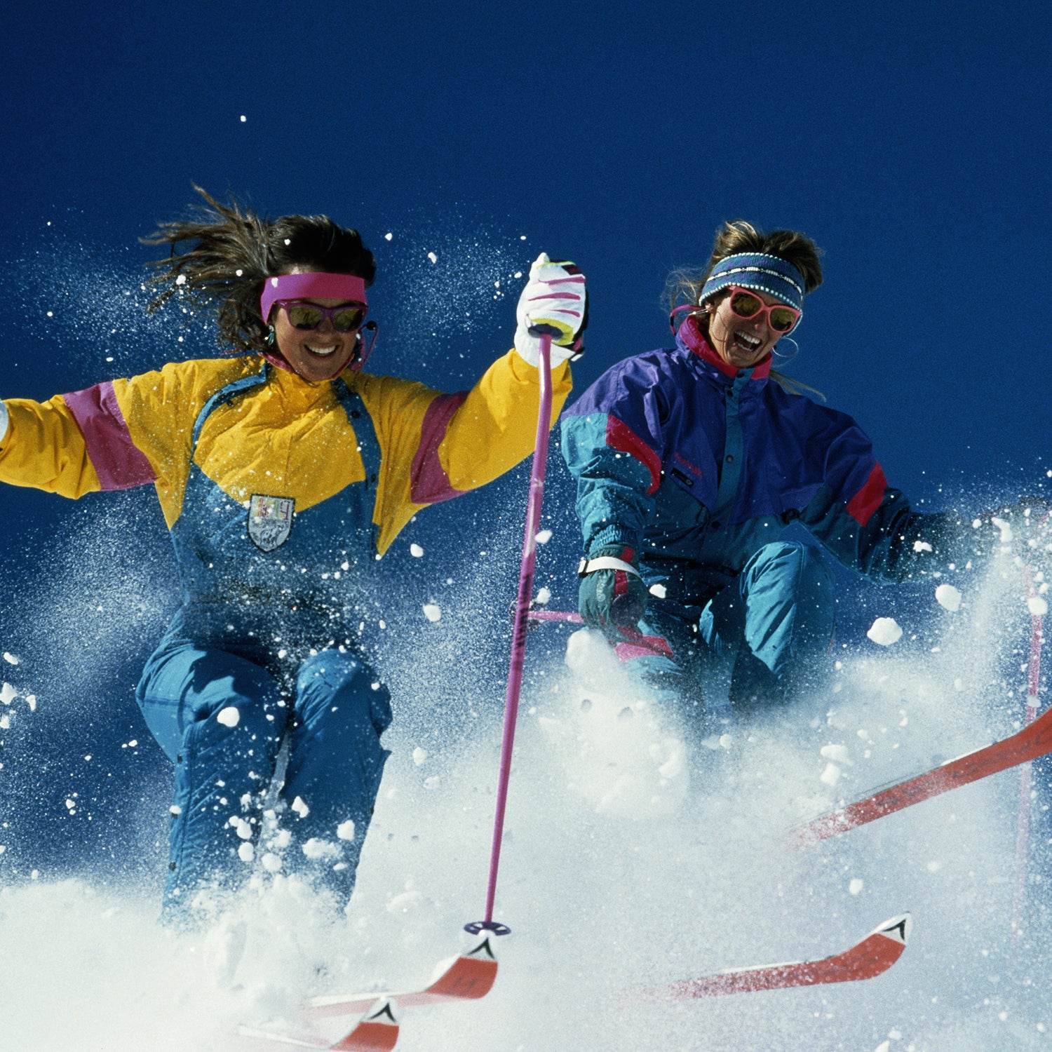 Two women skiing downhill, creating snow spray, low angle view