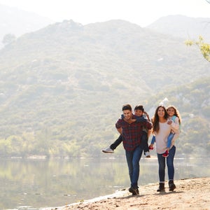 Parents piggybacking their young children by a mountain lake