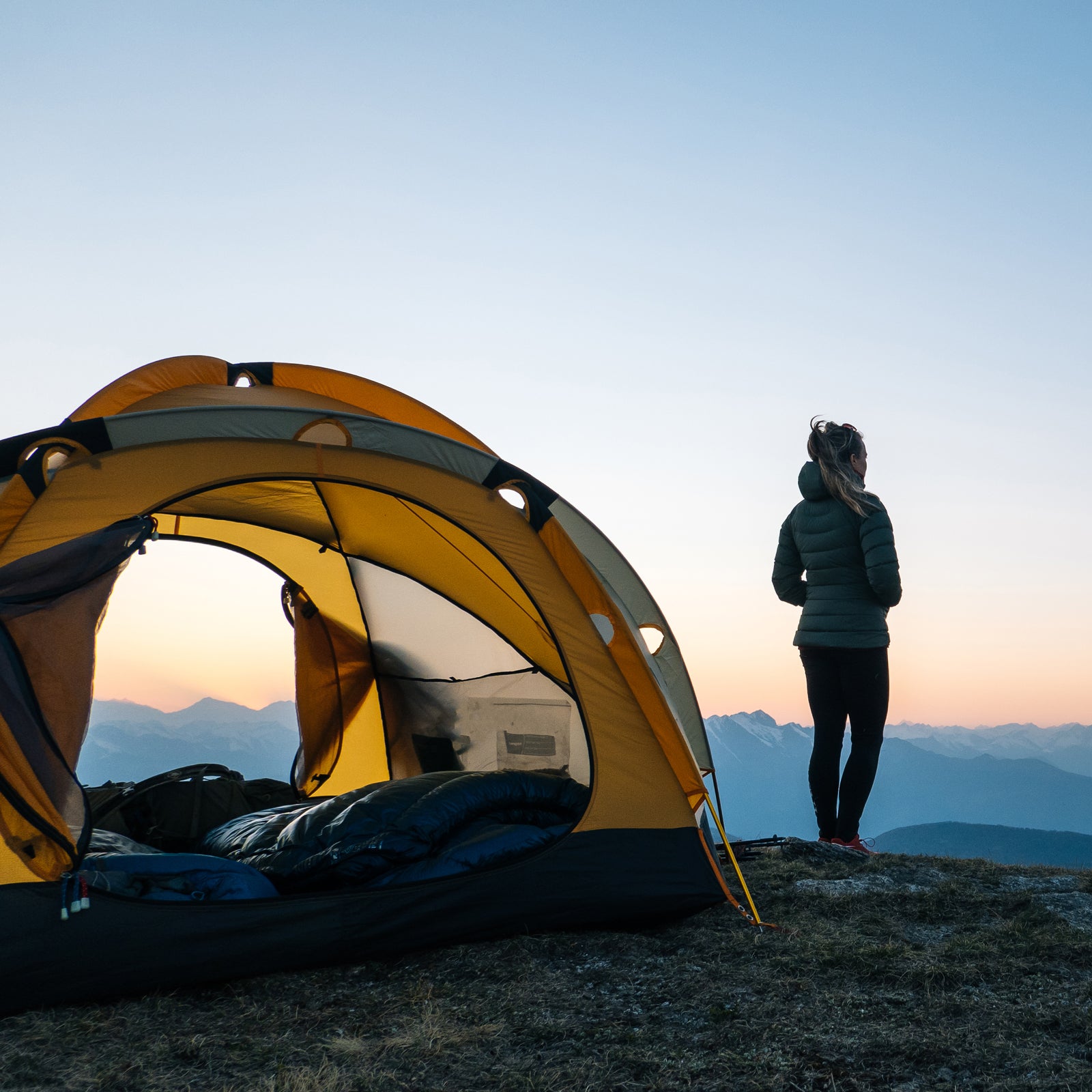 Young woman watches sunrise outside camping tent
