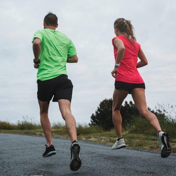 Motivated Young Couple Running Together Outside On Cold, Windy Day