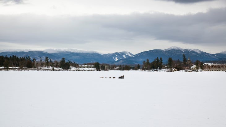 Dog sled in the distance on the frozen lake with mountains in the background. Lake Placid, NY