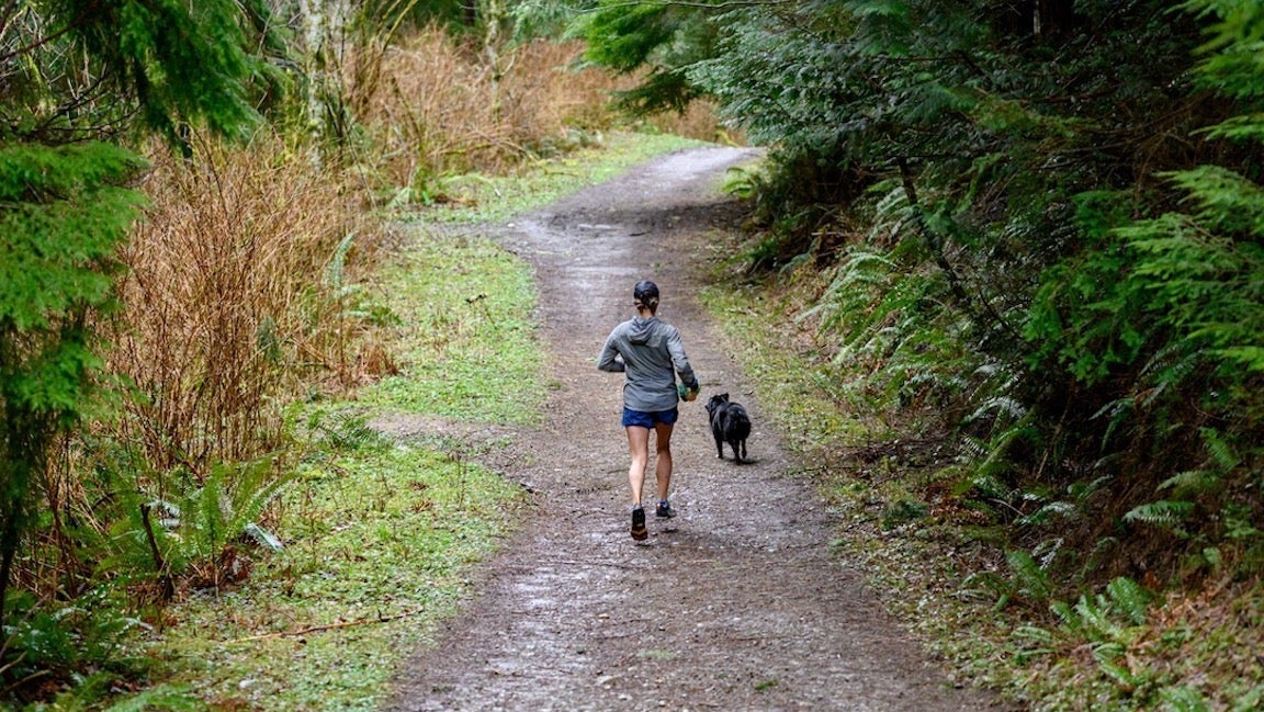 Woman running in green forest with a dog.