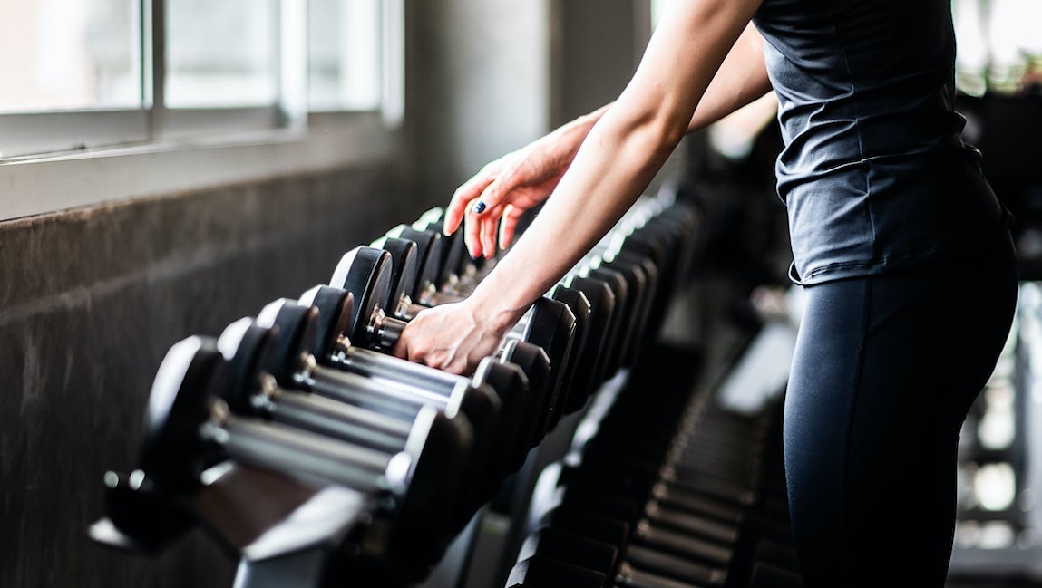 Young woman choosing dumbbell at a gym