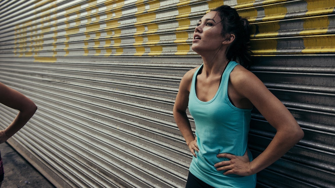 Woman runner who is tired leaning against parking garage shutter in exhaustion.