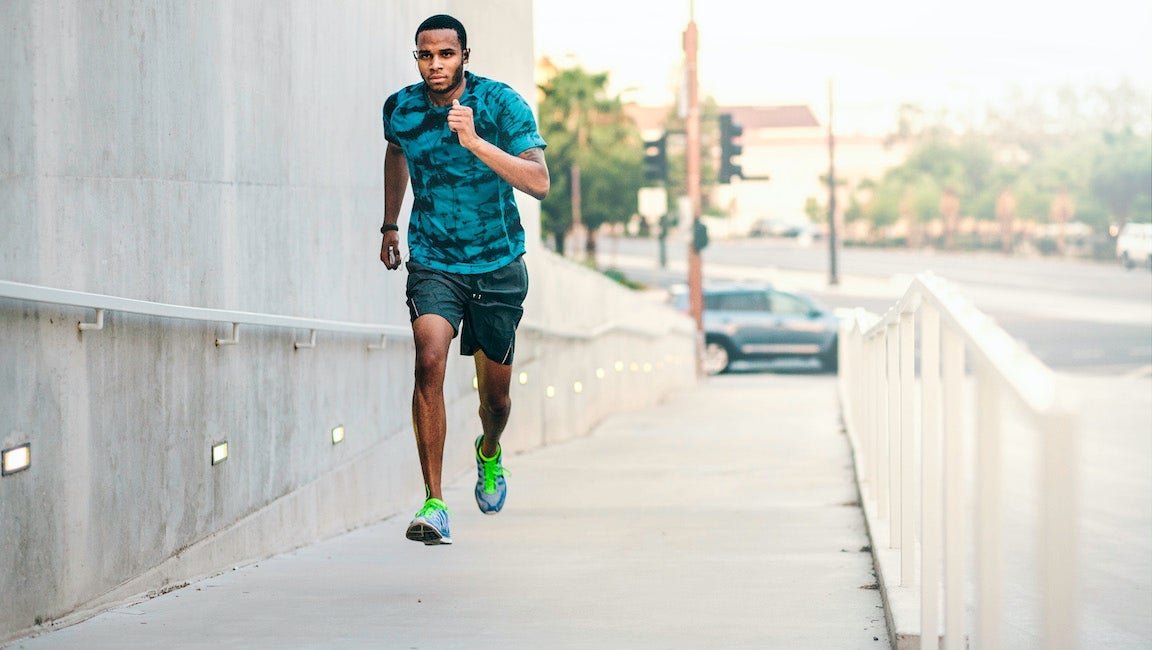 Young man running up city footbridge hill.