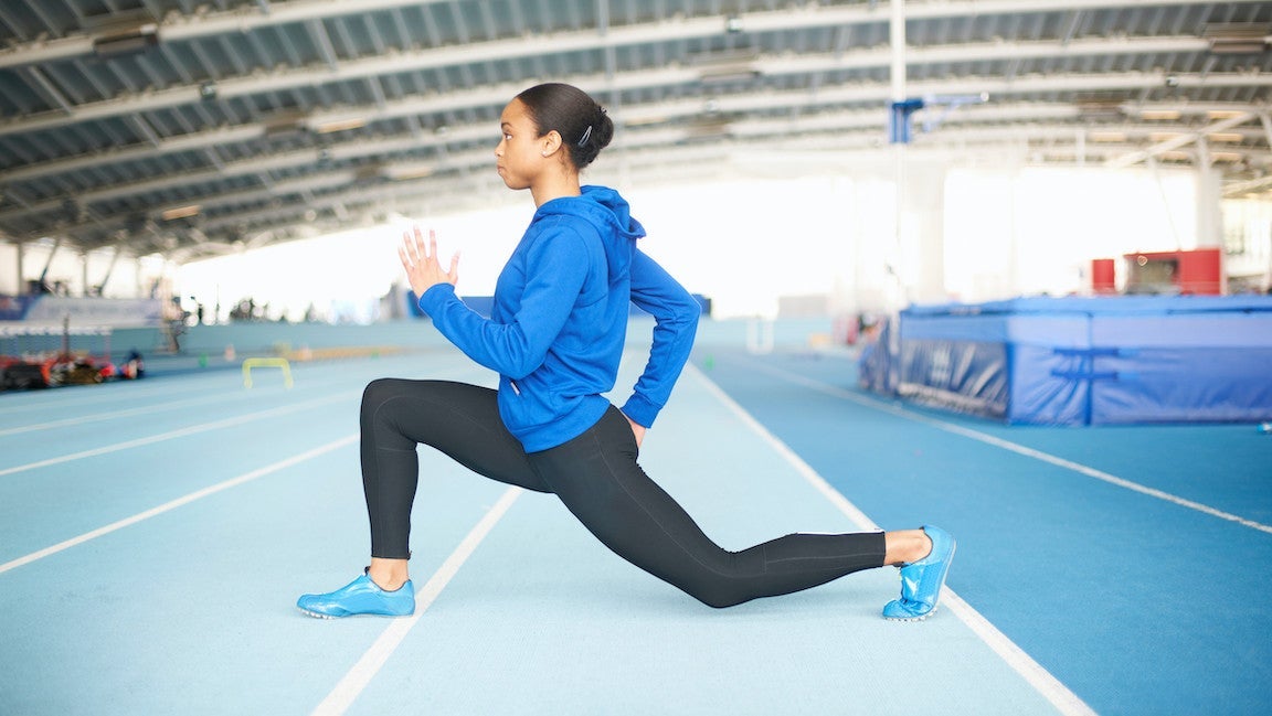 Young female athlete lunging in a gym by an indoor track.