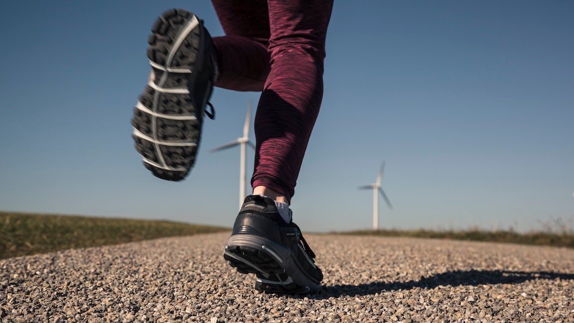 Young woman jogging on field way, wind wheels in the background.
