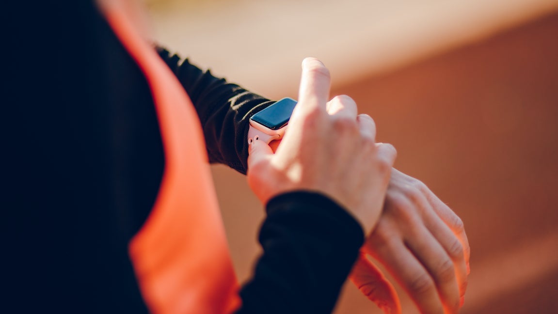 Close-up of young woman setting and checking smart watch on a race track.